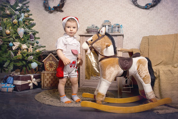 Fototapeta na wymiar A little boy plays with a horse-rocking around the Christmas tree
