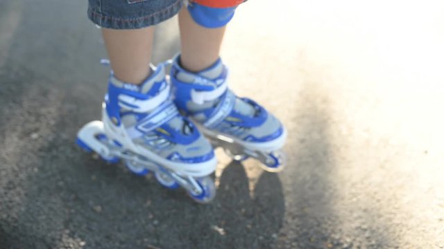 Legs of a boy learning roller skating on road.