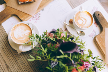 Still life with cup of coffee and flowers on wooden table.