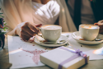 Hands of the bride and groom for a cup of coffee. Wedding bouquet on the table. Marriage concept.