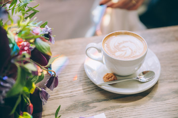 Still life with cup of coffee and flowers on wooden table.