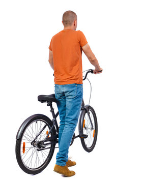back view of a man with a bicycle. Cyclist keeps the wheel of a bicycle.   backside view of person. Isolated over white background. The guy in a shirt standing with his bicycle.
