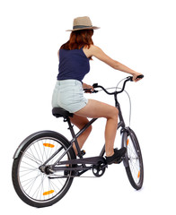 Fototapeta premium back view of a woman with a bicycle. cyclist sits on the bike. Rear view people collection. backside view of person. Isolated over white background. Beautiful girl in a hat and shorts on a bike.