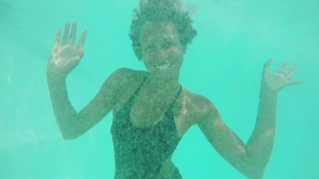 Cute African American female in black swimsuit diving in pool smiling laughing. Close up underwater footage in slowmotion