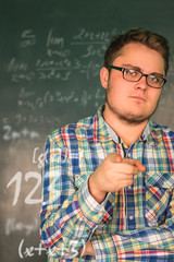 Full man in glasses close-up on a background blackboard with mathematical solutions of higher mathematics, he shows his finger at the camera. The man's face, looking at the camera. figures, numeral