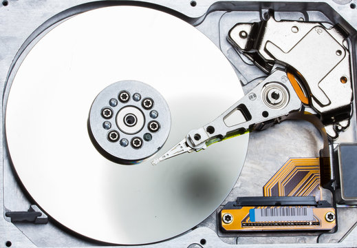 Top view of open hard disk drive showing actuator arm and reflective platter, representing data storage and computing technology.