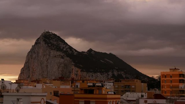 The Rock of Gibraltar with dramatic cloudy sky and birds flying above La Linea de la Concepcion cityscape during autumn day in Spain.