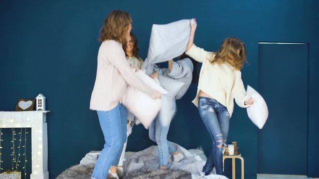 Four beautiful girls fight pillows each other . Girlfriends having fun and laugh in bedroom