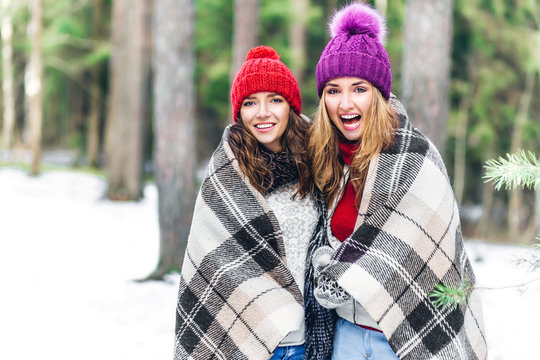 Two crazy friends girls roll oneself in a rug and walking in winter forest. emotional portrait of stylish portrait of pretty young hipster blonde and brown woman,get smile,pink hat,soft colors