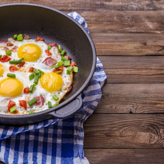 Fried eggs in pan with tomatoes and green fresh onion.