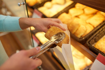 hand with tongs taking bun at bakery or grocery