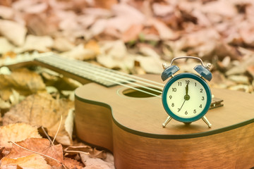 Retro Alarm on Ukulele Guitar on Autumn Leaves Background. Time