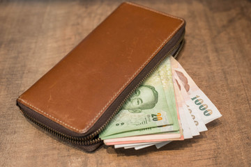Unzipped brown leather long wallet and Thai money on wooden tabl