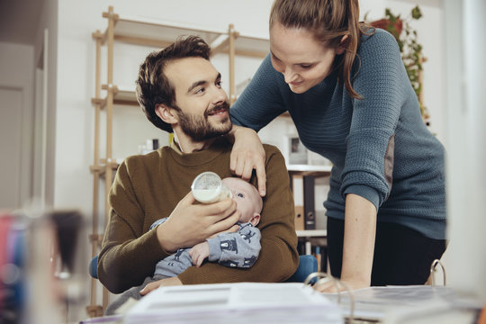 Mother looking at father feeding baby in home office