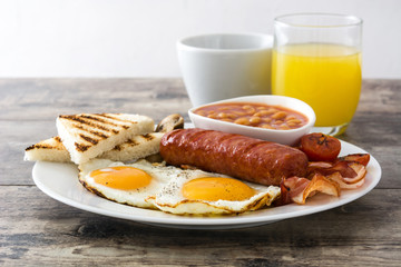 Traditional full English breakfast with fried eggs, sausages, beans, mushrooms, grilled tomatoes and bacon on wooden background

