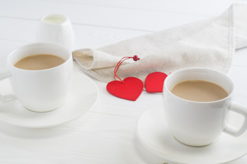 Romantic breakfast with couple white cups of coffee on white wooden background.  A romantic coffee for a couple in a cafe on St. Valentine's Day. Cocoa or coffee with milk, clouse up.