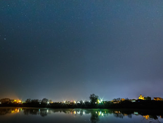 Starry sky over the lake. Street lights reflected in the water.