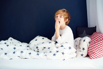 cute yawning kid in pajamas sitting in bed © Olesia Bilkei