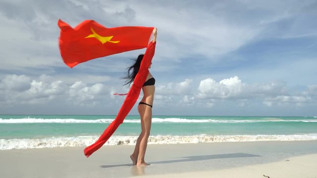 Young woman in red dress stand on caribbean beach with vietnamese flag at her arms