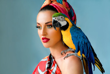 Portrait of young attractive woman in african style with ara parrot on her showlder on colorful background - obrazy, fototapety, plakaty