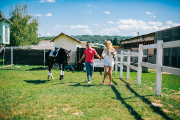 Young couple stay and walking near black horse at green farm