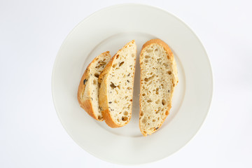 slices of bread on a white oval-shaped top view. European bread loaf of wheat flour with the addition of olive slices cut into pieces on a white plate