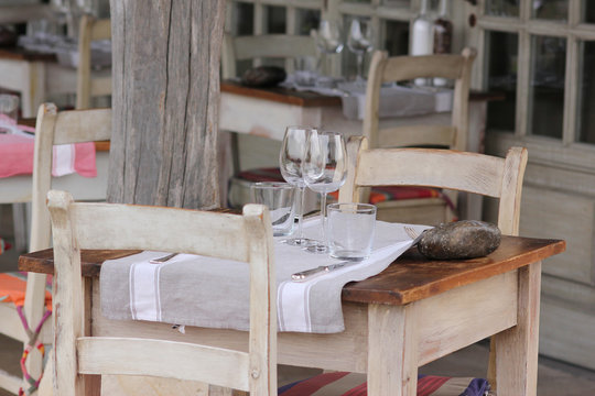Table de restaurant en terrasse avec verre à vin, nappe et couverts.