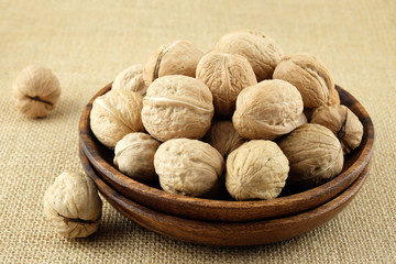 Walnuts in a wooden plate on burlap cloth.
