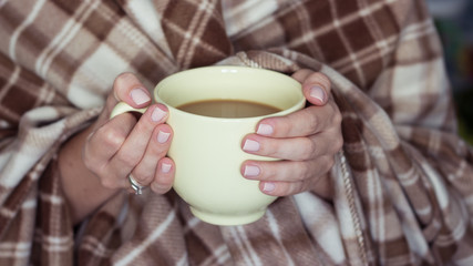 Young woman wrapped in a plaid, and holding a cup of hot coffee. Cozy Fall. Female hand holding a mug of hot coffee.