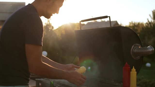 Caucasian man preparing corn to be fried on barbecue grill outdoors in slowmotion