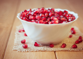 Pomegranate seeds in a bowl on a wooden table.