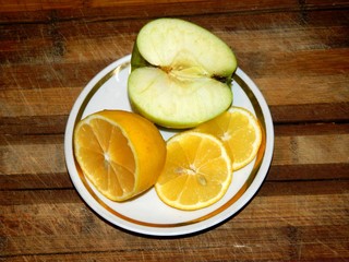 on a wooden chopping board in a white saucer with golden rim is half green apple and lemon and two...