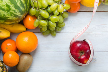 Apple and measuring tape with fruits on wooden board