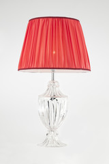 lampada da tavolo in cristallo e paralume in seta rossa, su fondo bianco.