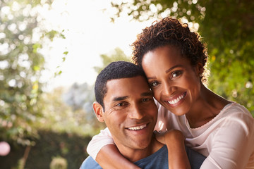 Fototapeta premium Young black couple piggyback in garden looking at camera
