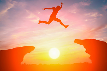 Silhouette of man jump over the cliff obstacle in sunset - obrazy, fototapety, plakaty
