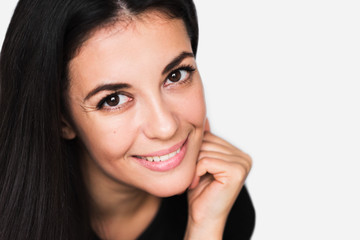 Close up portrait of brunette cute woman with beauty smile, with hand face. Young happy pretty woman wearing black sweater on light grey background. Positive and happiness mood.