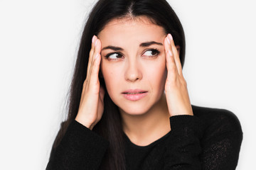 Close up portrait of brunette pretty woman with headache touching her temples look at one side. Beautiful woman stressed and worry in black sweater on light grey background. Healthcare and medicine.