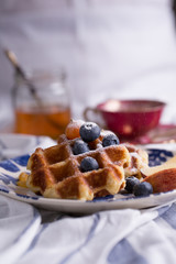 Blueberry apple waffle with honey set on a dish with a chef's hand holding spoon for a jar of honey ready to serve.