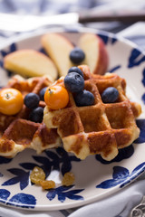 Blueberry apple waffle with honey set on a dish with a chef's hand holding spoon for a jar of honey ready to serve.