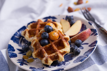 Blueberry apple waffle with honey set on a dish with a chef's hand holding spoon for a jar of honey ready to serve.