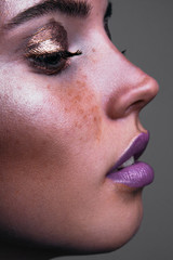 Fashion portrait of a young woman with creative bronze makeup and violet lips shot in studio
