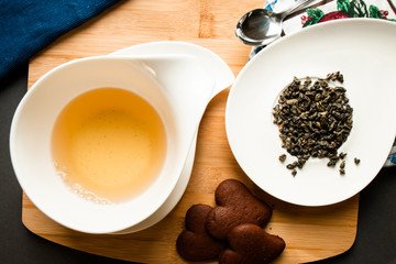 green tea leaves next to a cup of tea served with chocolate cookies