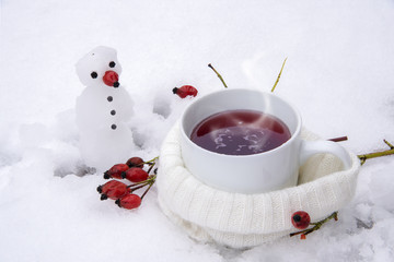 Obraz na płótnie Canvas Hot tea with red rose hips in the snow and a little snowman, vitamin winter drink agains flu