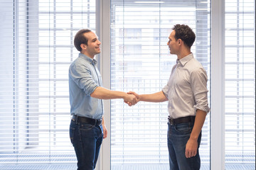 Two colleagues dressed casually shaking hands in modern office interior