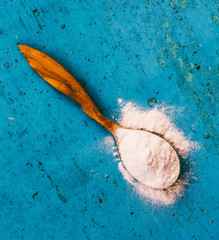 wooden spoon with flour at the old blue grunge background, closeup, top view