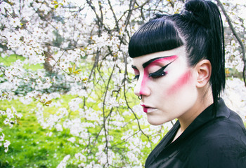 Mujer joven vestida y maquillada como una geisha celebrando la primavera en un parque lleno de cerezos en flor 