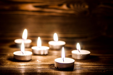 Small decorative candles burn in the dark. Candles stand on a wooden surface of brown.