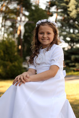 Śliczna dziewczynka w białej sukni siedzi na trawie. - obrazy, fototapety, plakaty