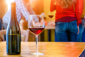 Friends drinking at home with red wine glass and bottle foreground on rustic table - Group of teenagers house party background with beverage close up as  concept of youth alcohol abuse